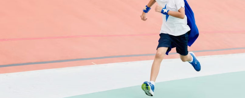 A child in a blue cape and a star-emblazoned shirt sprinting across a running track.